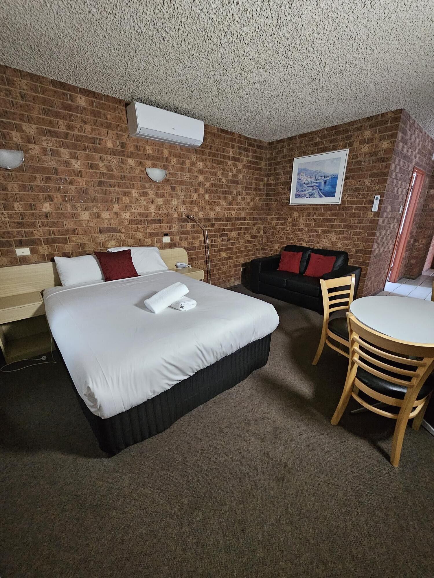 Habitación de hotel con una cama grande, una mesa de madera, un sofá negro y una pared de ladrillo.