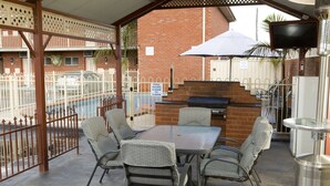An outdoor patio with a pool table, wicker chairs, and a barbecue grill.