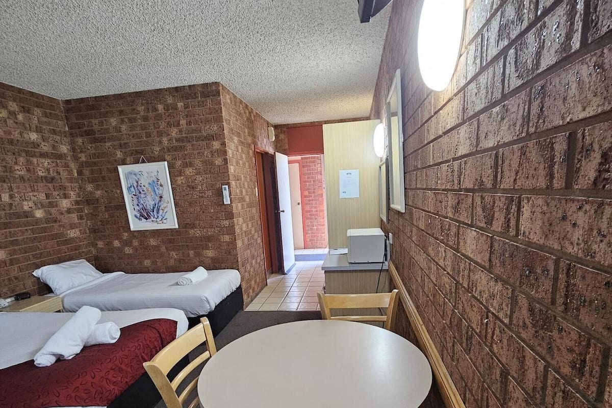 A room with two beds, a round table, and a brick wall.