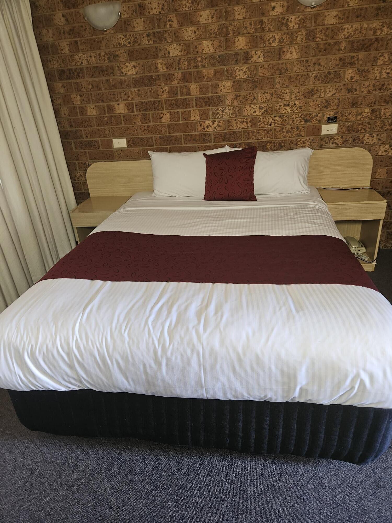 A hotel room with a large bed, a wooden headboard, a nightstand, and a brick-patterned wall.