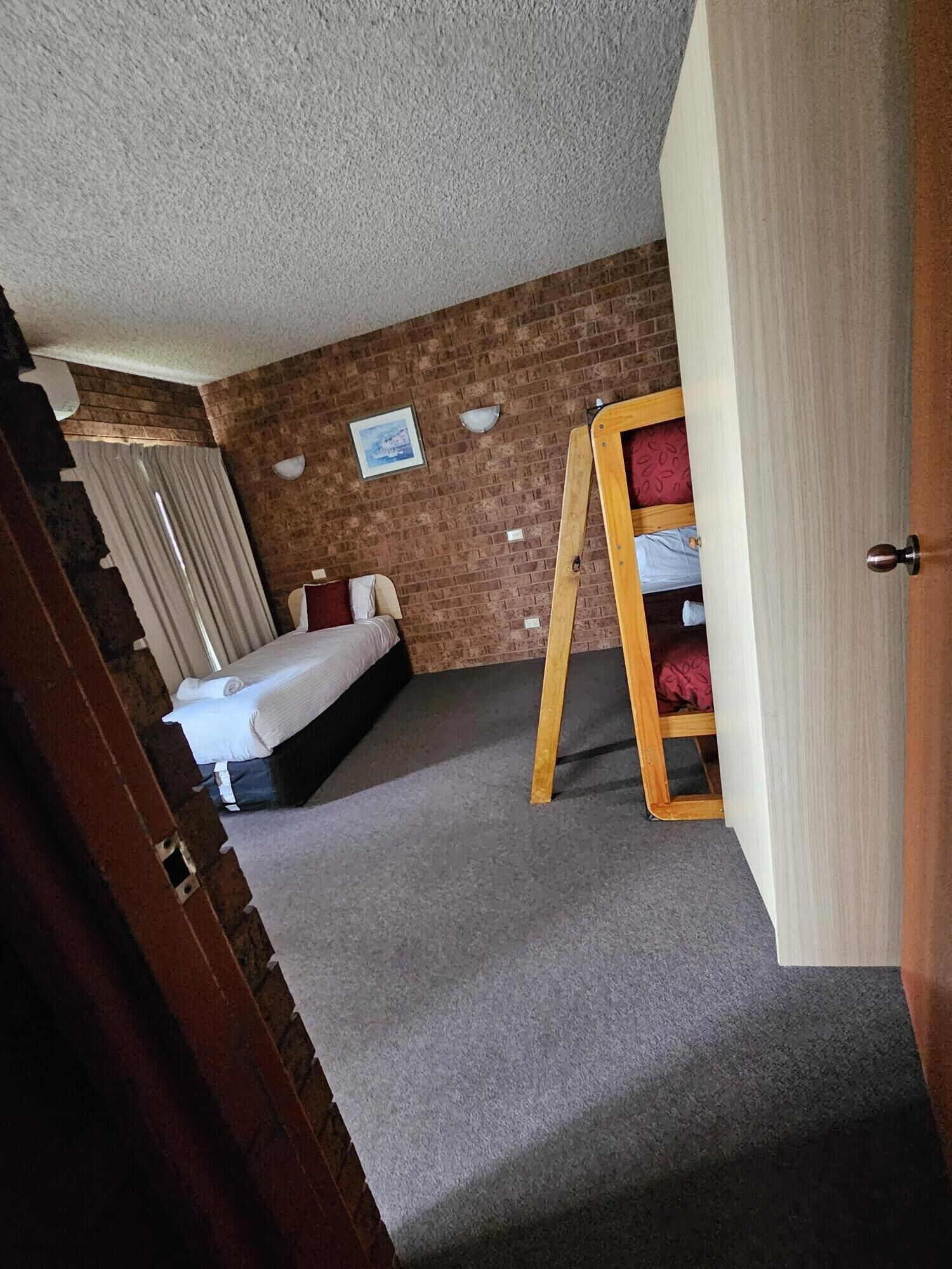 Una habitación con cama, una escalera de madera, una pared de ladrillo y una puerta.