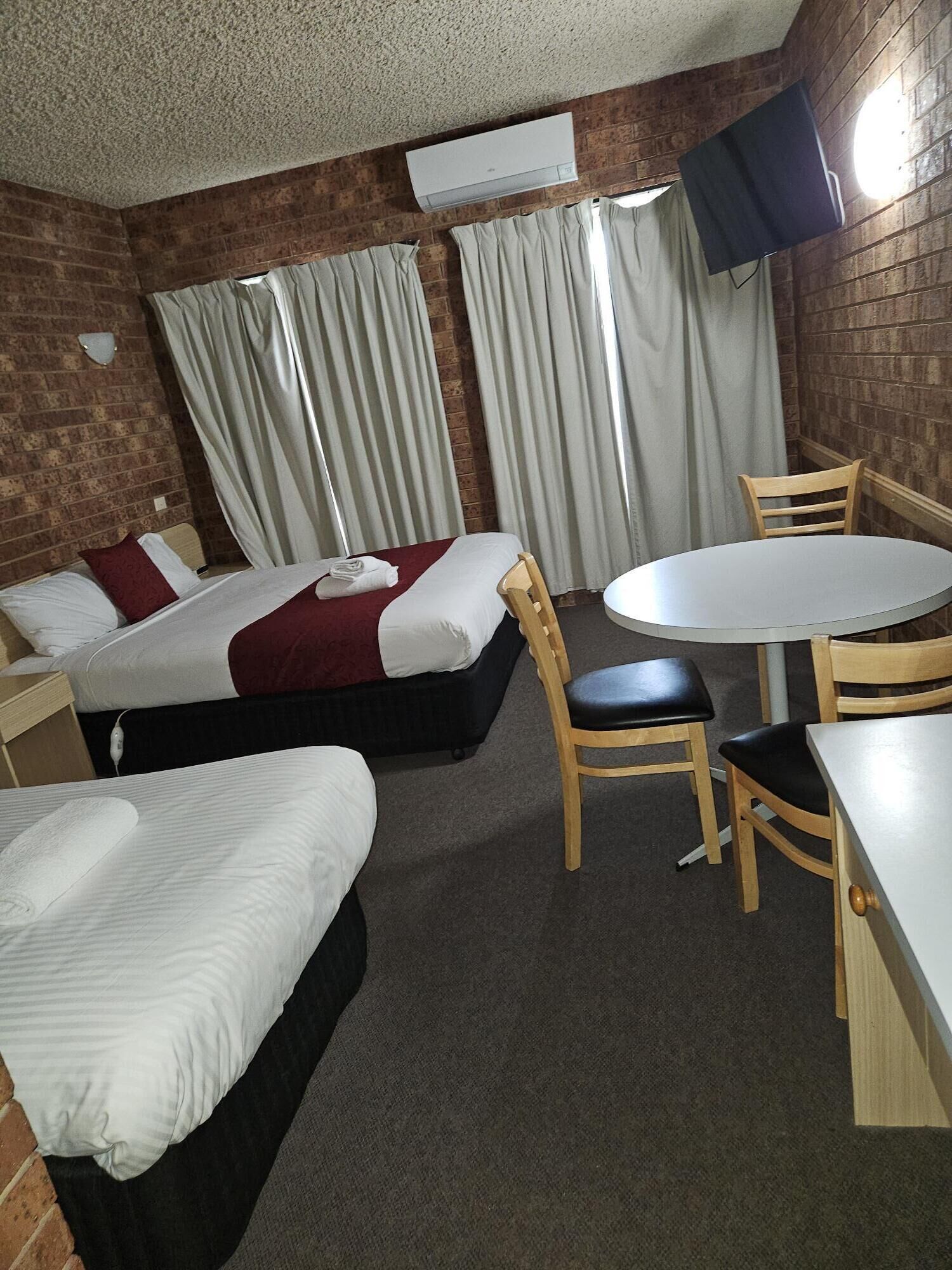 A hotel room with two single beds, a small round table, and a TV mounted on the wall.