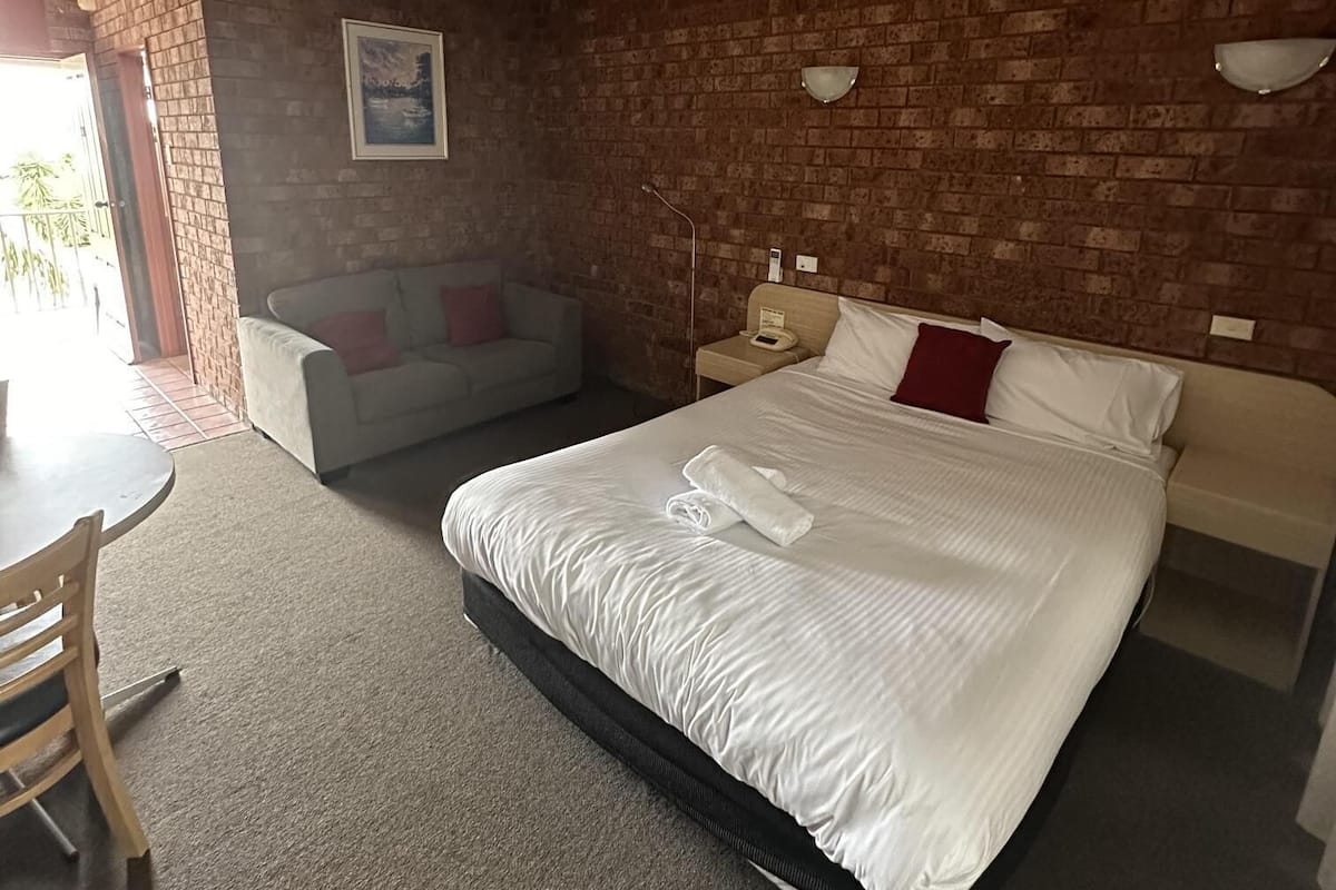 A hotel room with a large bed, a small sofa, a desk with chairs, and a brick wall.