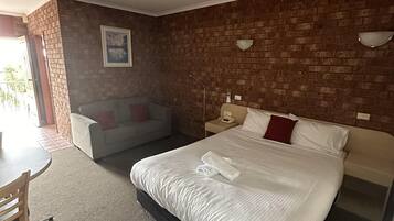 Une chambre d’hôtel avec un grand lit, un petit canapé, un bureau avec des chaises et un mur en briques.