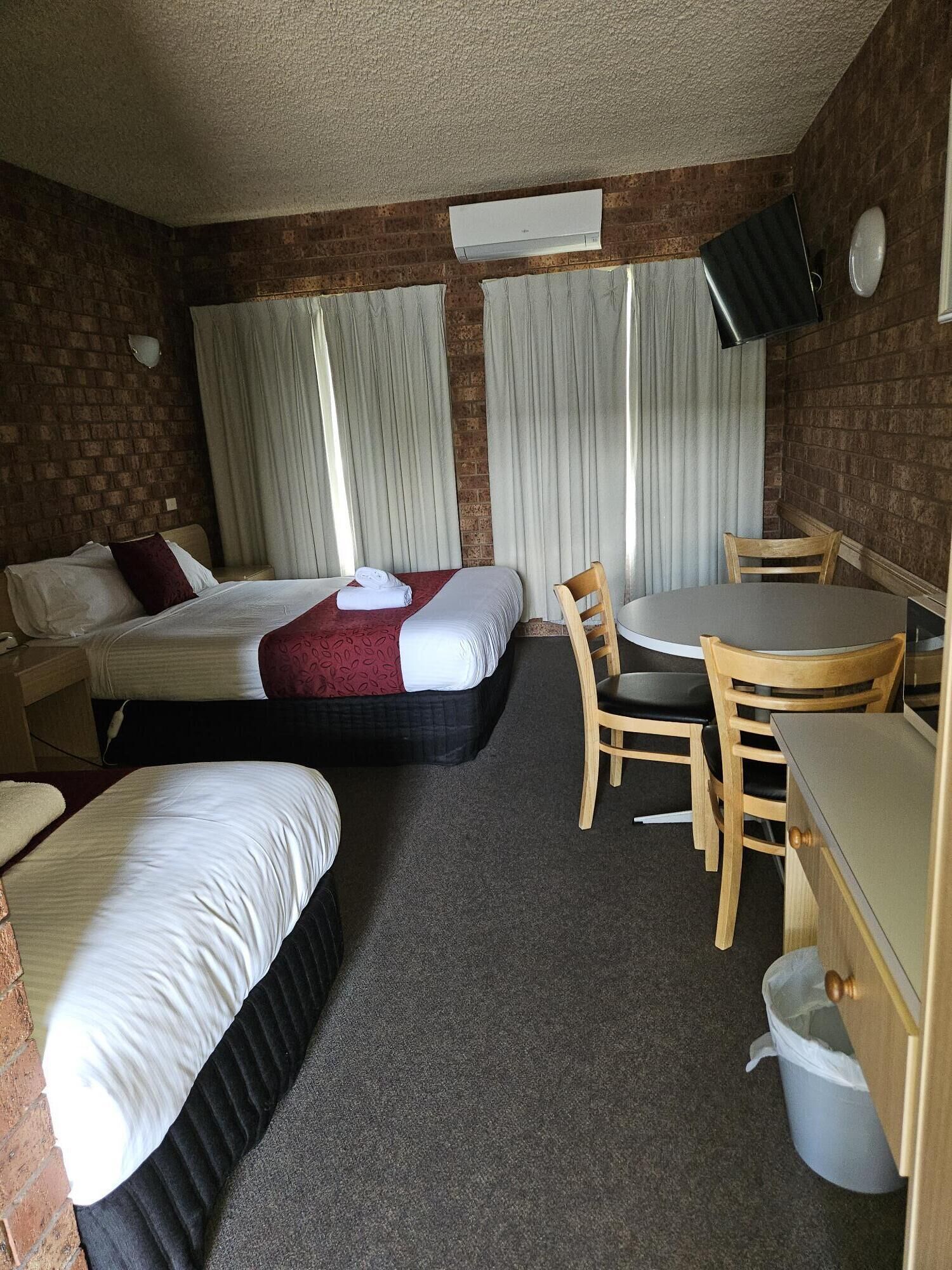 Habitación de hotel con dos camas, una mesa de comedor con sillas, un escritorio pequeño y un cubo de basura.