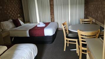 Habitación de hotel con dos camas, una mesa de comedor con sillas, un escritorio pequeño y un cubo de basura.