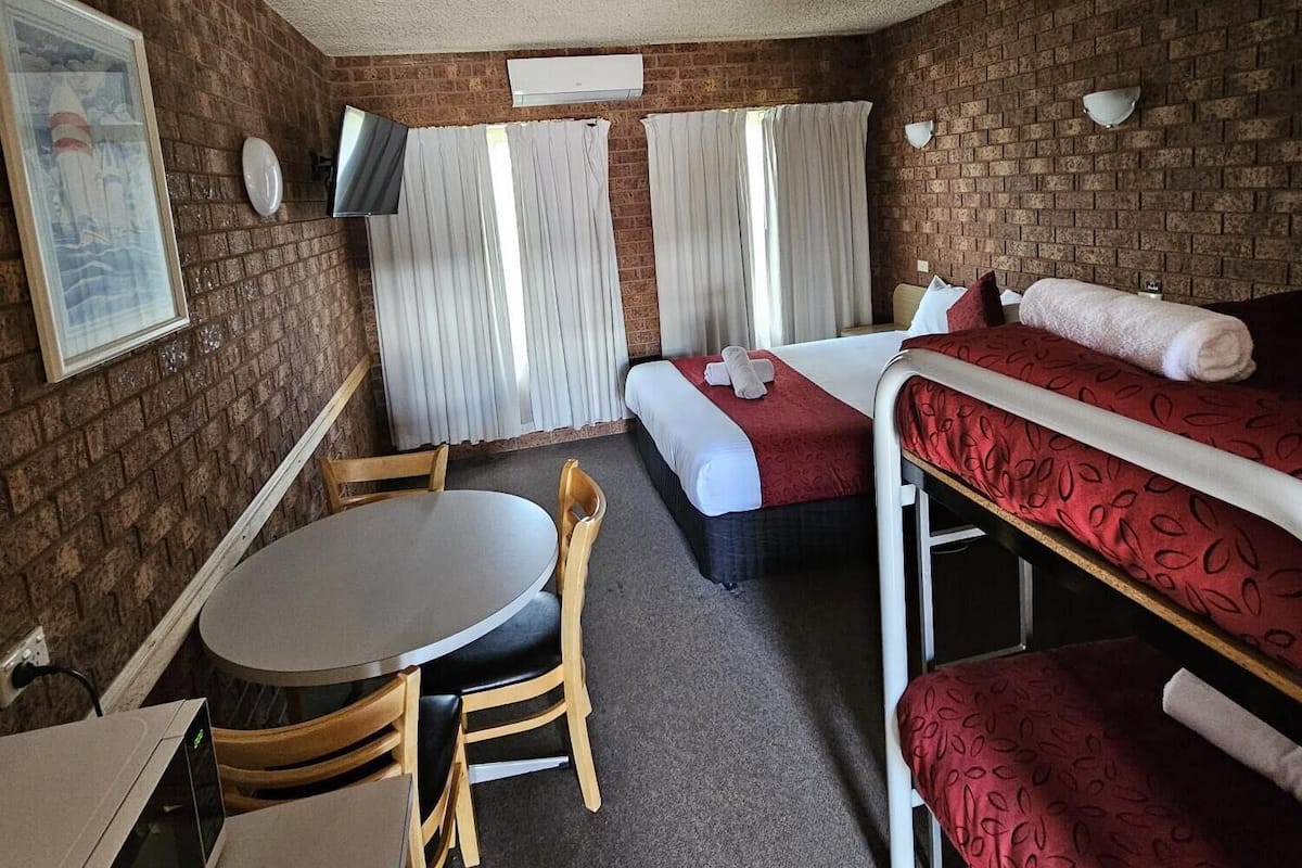 A compact hotel room with a bunk bed, a single bed, a small table with a chair, and a television.