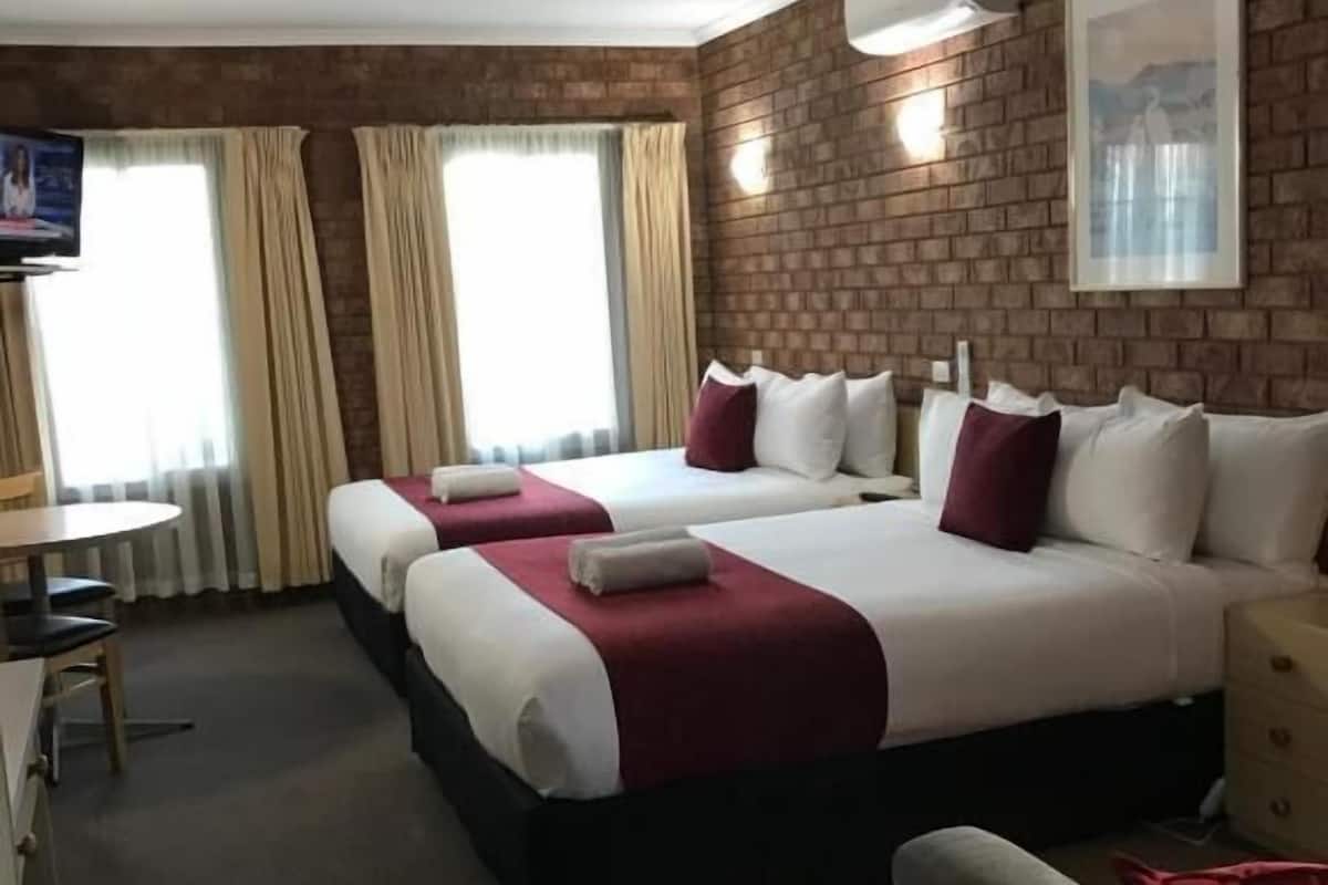 A hotel room with a large bed, two bedside tables, a TV, and a brick wall.