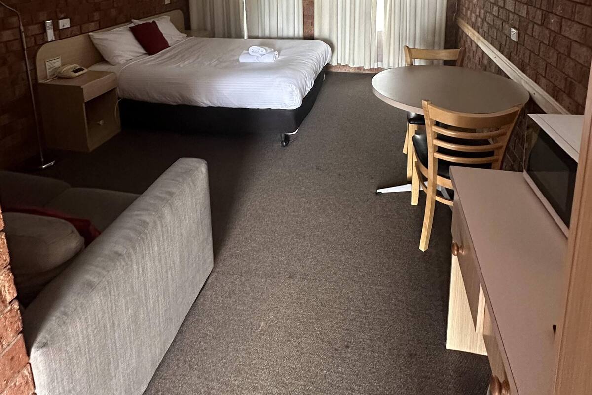 A hotel room with a bed, a desk, a chair, a sofa, and a TV.