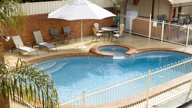 A swimming pool with a white fence, lounge chairs, and a table with chairs.