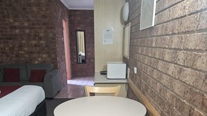 A room with a bed, a sofa, a round table with chairs, and a brick wall.