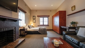 A room with a fireplace, a bed, a desk, a couch, and a television. - The Civic Hotel (Inglewood)