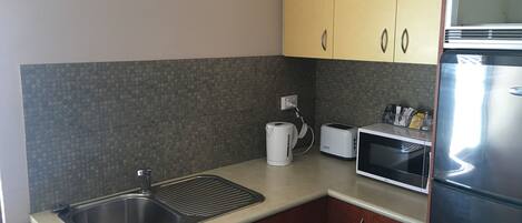 A modern kitchen with a stainless steel sink, a kettle, a toaster, and a microwave.