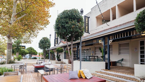 An outdoor patio with wooden tables and benches, surrounded by brick flooring and potted plants. - The Civic Hotel (Inglewood)