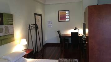 A hotel room with a bed, a desk, a chair, and a small table.
