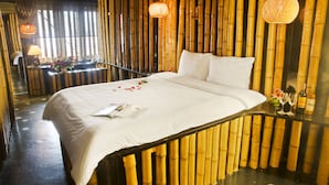 A bed with white linens, a bedside table with a lamp, and a wall with vertical bamboo panels.