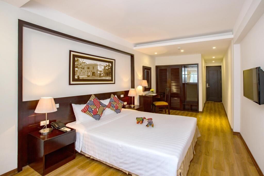 A hotel room with a bed, bedside table, lamp, and a framed picture on the wall.
