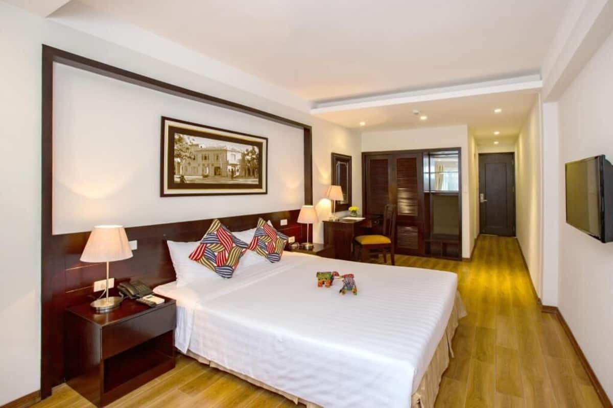 A hotel room with a bed, bedside table, lamp, and a framed picture on the wall.