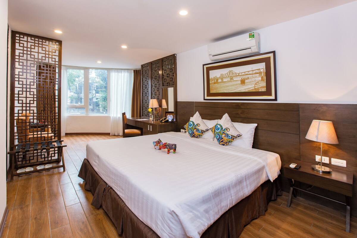 Une chambre d’hôtel avec un grand lit, un bureau, une chaise, un paravent décoratif et un tableau encadré au mur.