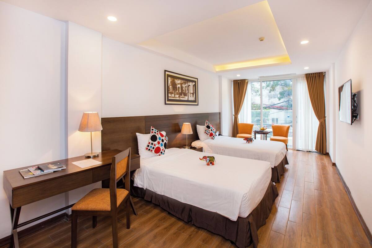 Une chambre d’hôtel avec deux lits, un bureau, une chaise, une lampe et une vue sur l’extérieur.