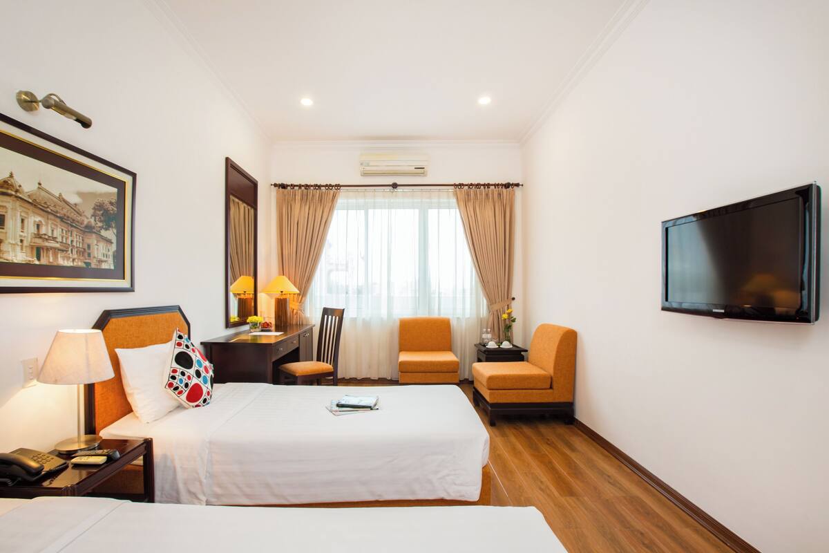 Une chambre d’hôtel avec deux lits, un bureau avec une lampe, une chaise, une télévision et un tableau au mur.