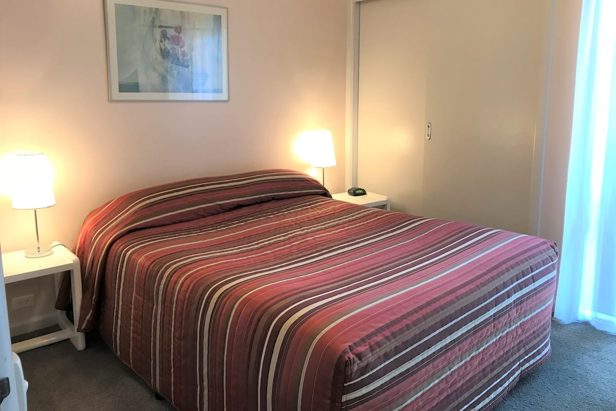 A hotel room with a bed, two bedside tables with lamps, a painting on the wall, and a door.