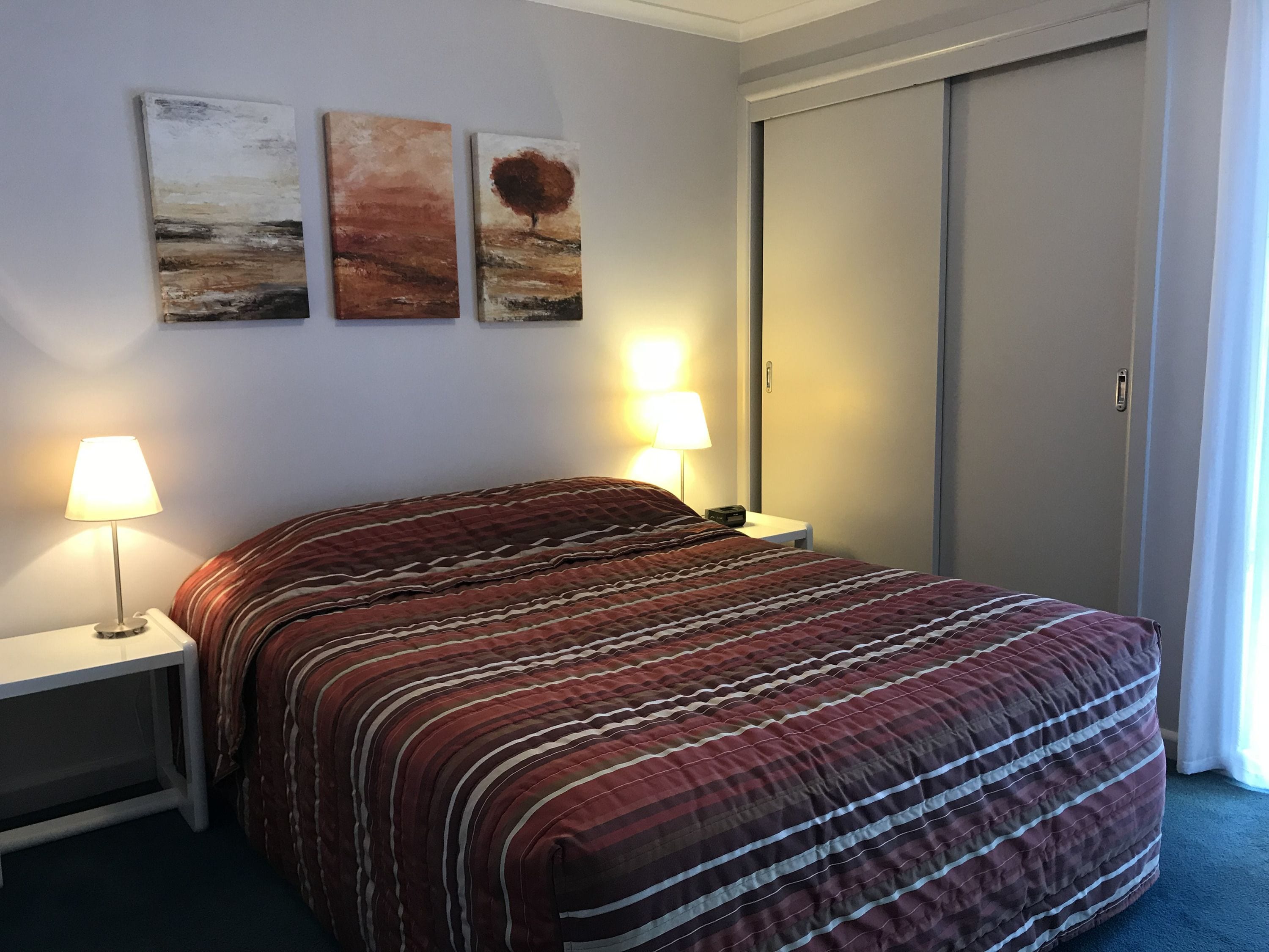 Une chambre d’hôtel avec un lit, deux lampes de chevet et trois tableaux au mur.