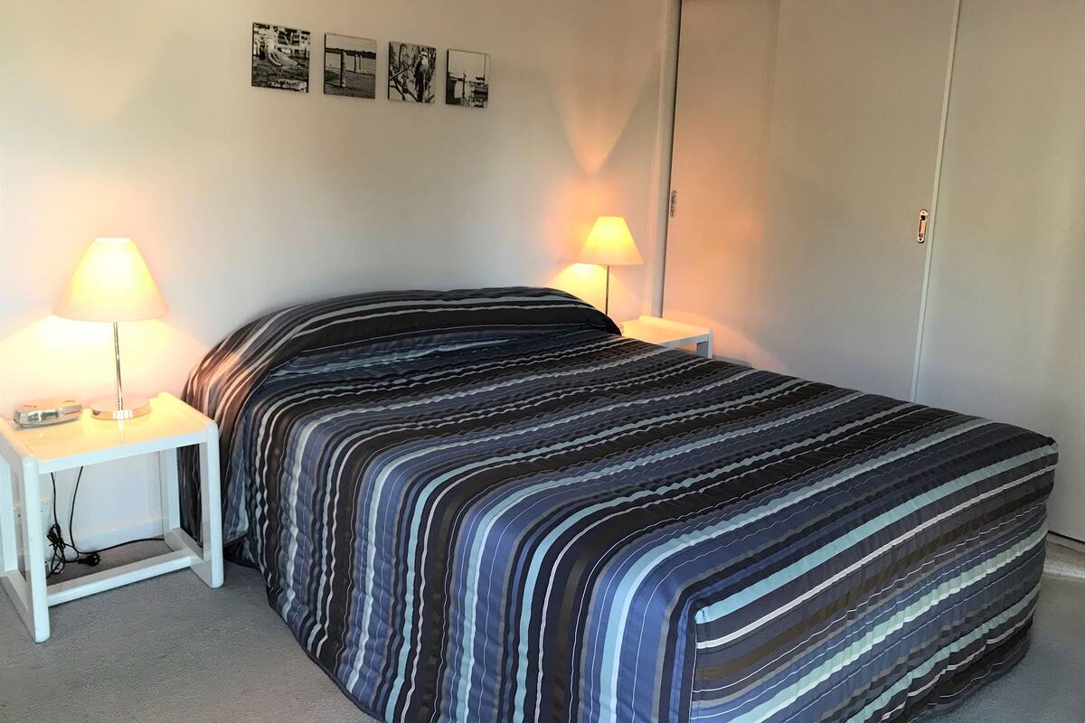 A bedroom with a striped bedspread, two bedside tables with lamps, and a closet.