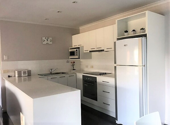 Una cocina moderna con armarios blancos, microondas integrado, estufa y refrigerador.