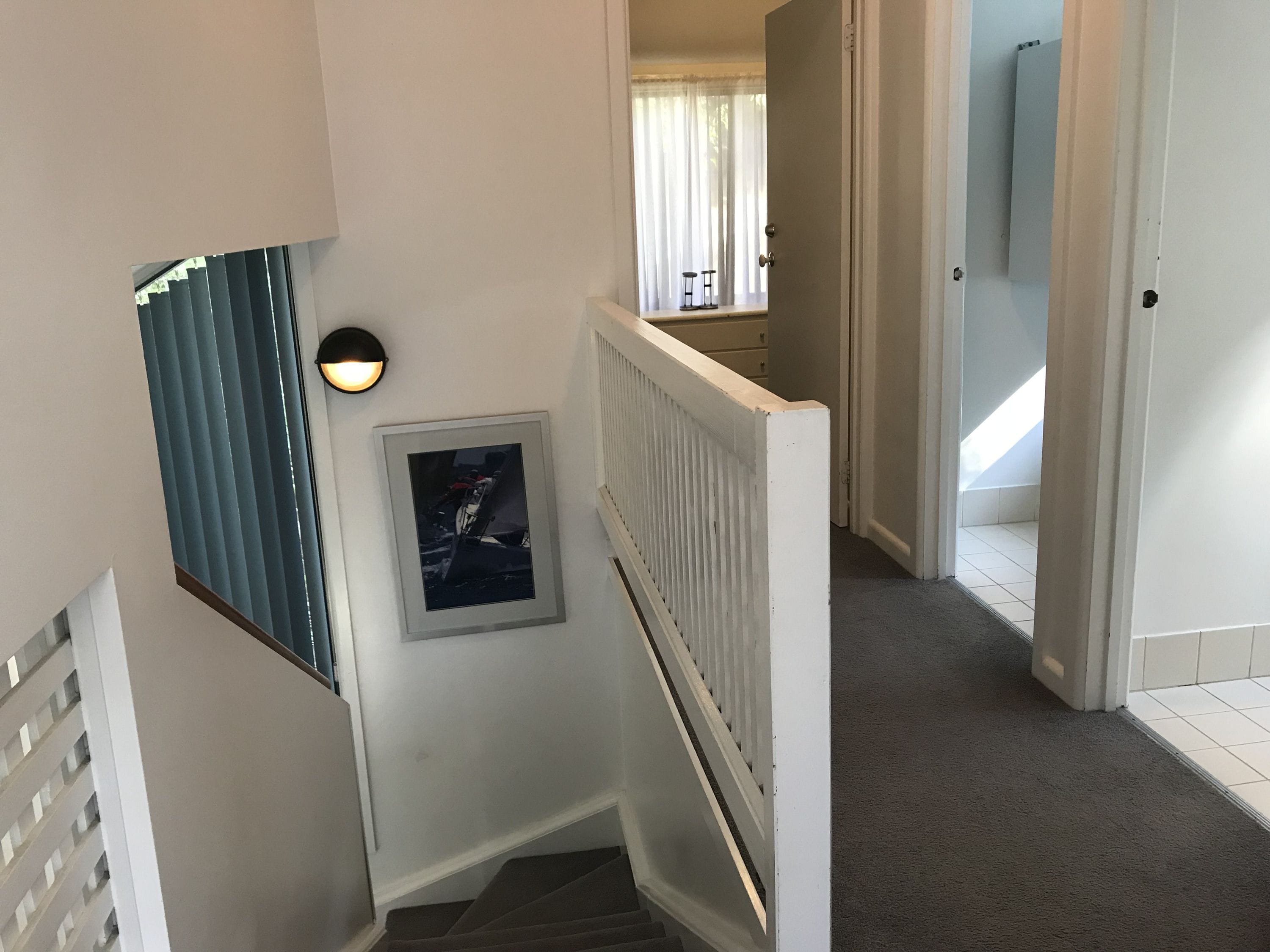A staircase with a white handrail, a framed picture on the wall, and a window with blinds.