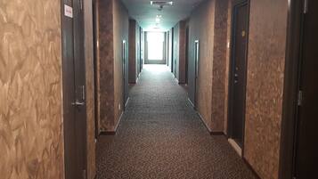 A hotel hallway with patterned carpet, wooden walls, and doors on both sides.