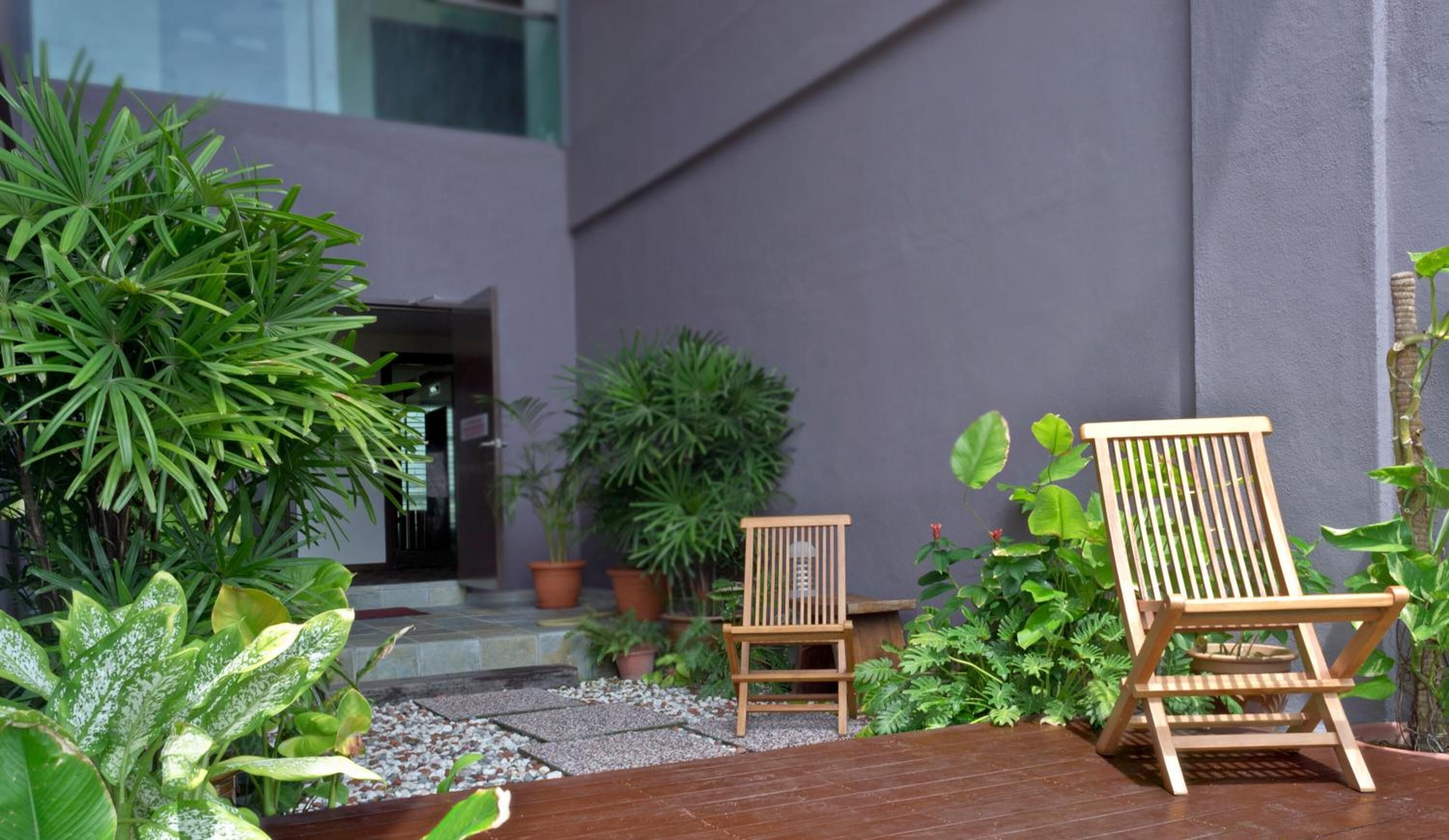 Una terraza de madera con dos sillas de madera, rodeada de plantas en macetas y un pequeño jardín.