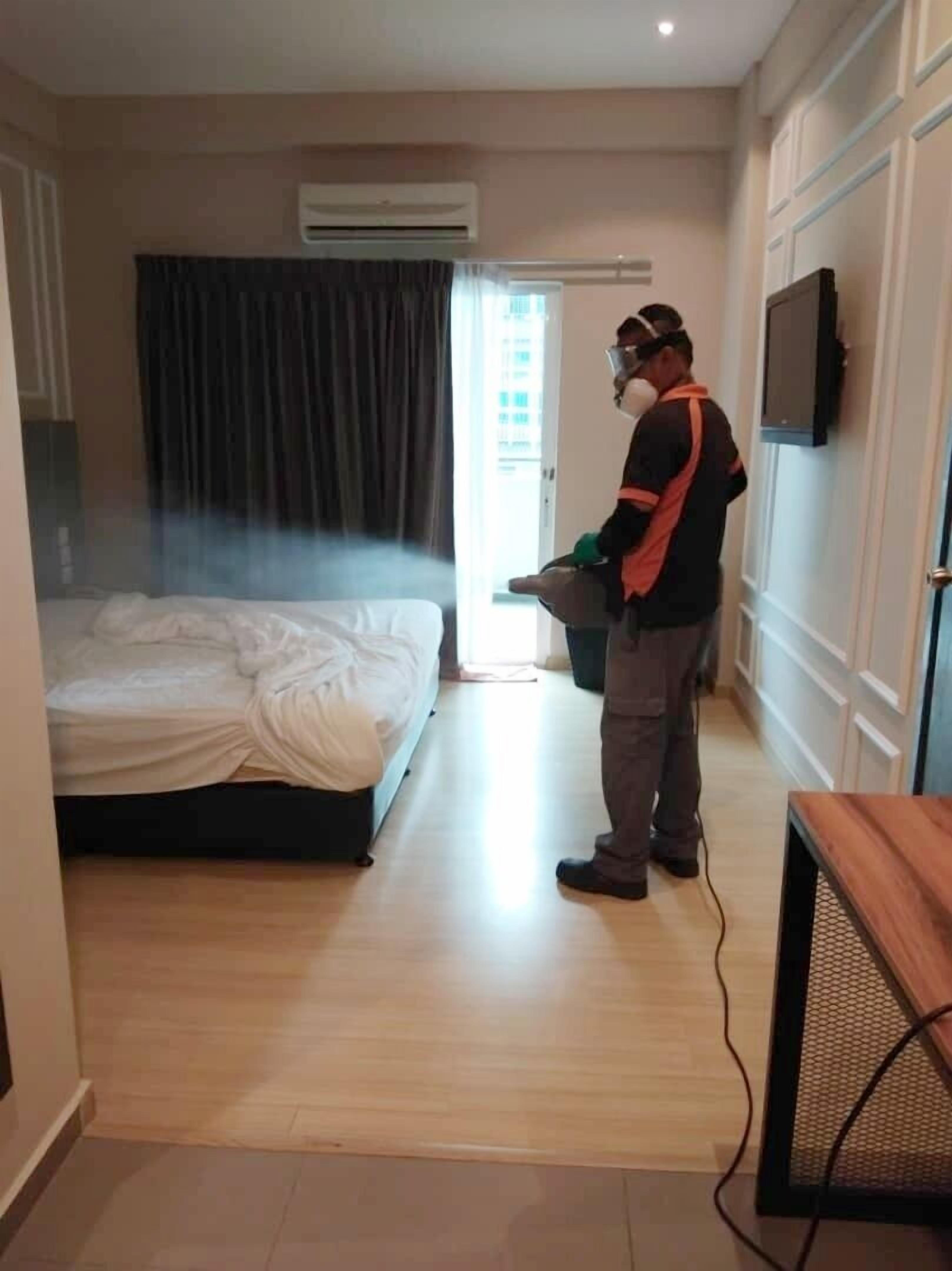 Una habitación de hotel con cama, equipo de aire acondicionado, televisor en la pared y una persona usando mascarilla y guantes.