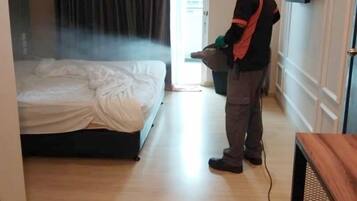Una habitación de hotel con cama, equipo de aire acondicionado, televisor en la pared y una persona usando mascarilla y guantes.