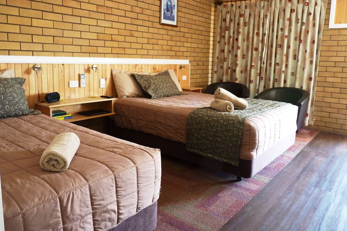 A hotel room with two beds, a wooden headboard, a brick wall, a framed picture, and a window with curtains.