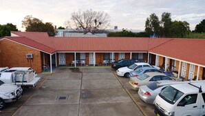 Un motel con techo rojo, una zona de estacionamiento techada y varios coches aparcados en el estacionamiento.