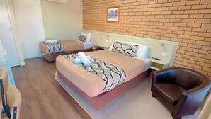 Una habitación de hotel con dos camas, una silla, una mesita y una pared de ladrillo.