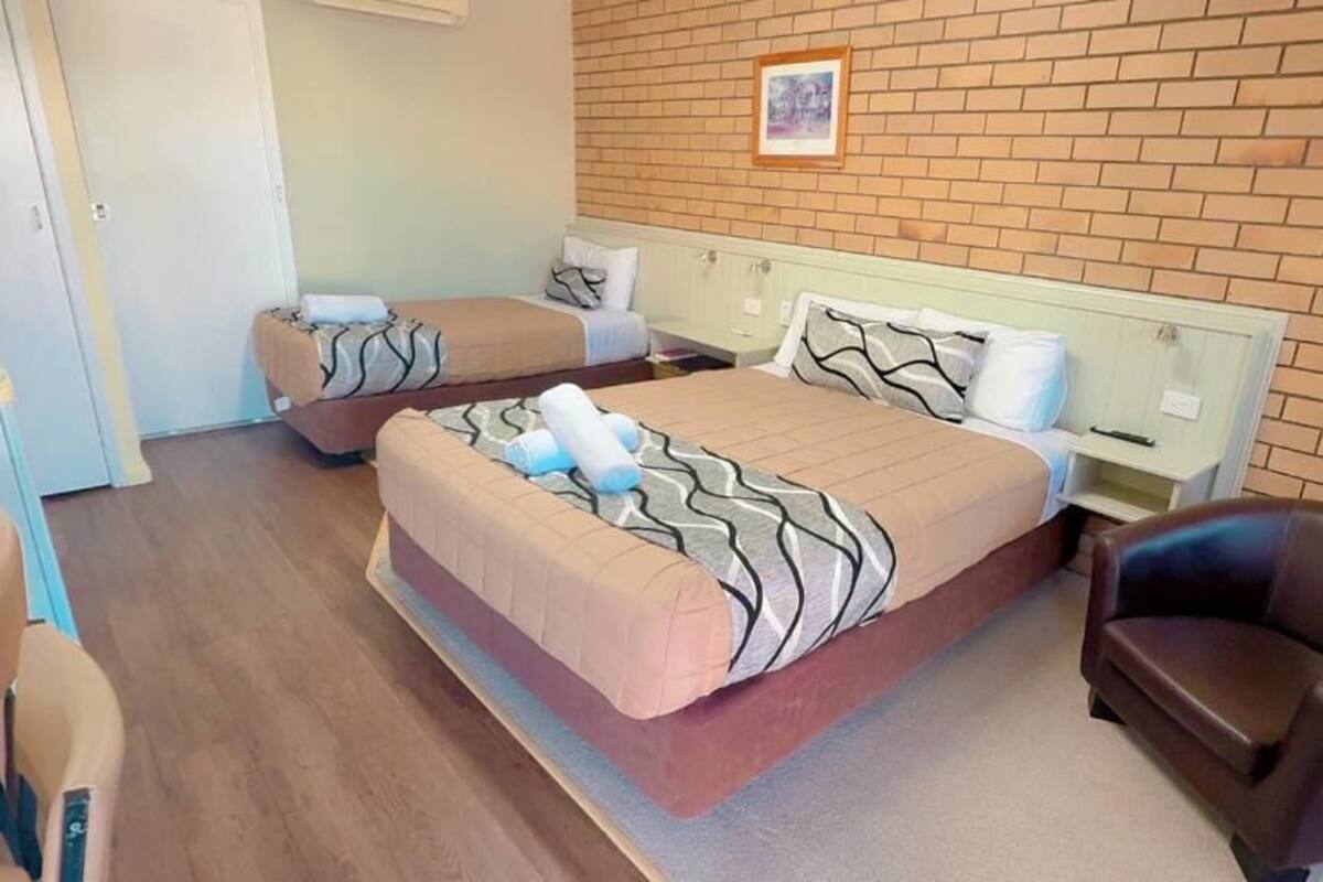 A hotel room with two beds, a chair, a small table, and a brick wall.
