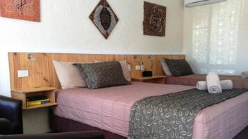 Una habitación de hotel con dos camas, cabeceros de madera y una ventana con cortinas translúcidas.