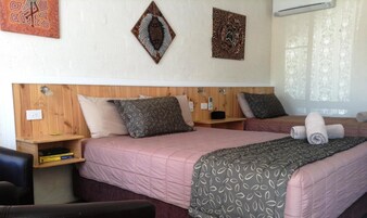Una habitación de hotel con dos camas, cabeceros de madera y una ventana con cortinas translúcidas.