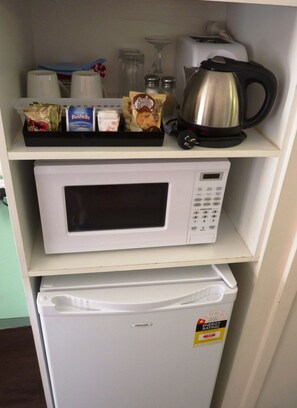 Una kitchenette equipada con microondas, tostadora, tetera y diversos alimentos en la estantería.