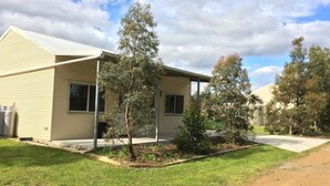 Une maison de plain-pied avec un toit en pente, un porche à l’avant et un petit jardin devant, agrémenté d’un arbre et de quelques arbustes.