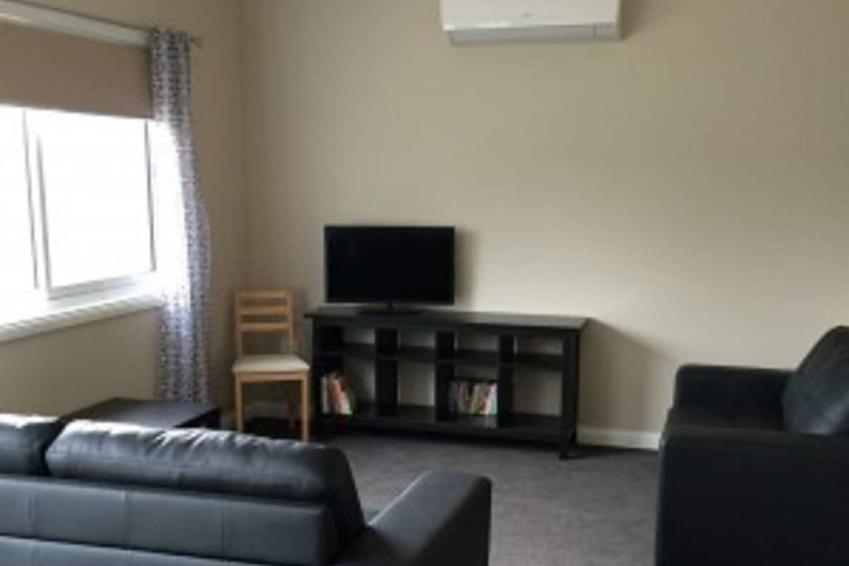 Een woonkamer met een donkergrijze bank, een televisie op een dressoir en een boekenkast.