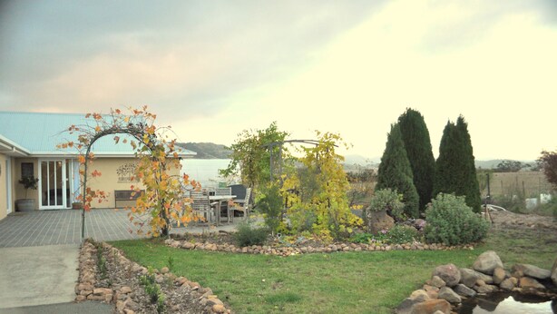 Un jardin résidentiel agrémenté d’une terrasse, d’un petit étang et offrant une vue sur une étendue d’eau.