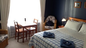 Une chambre d’hôtel avec un lit, une chaise, une table et une fenêtre avec des rideaux.