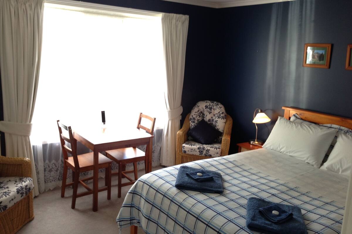 Een hotelkamer met een bed, een stoel, een tafel en een raam met gordijnen.