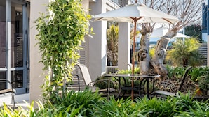 An outdoor seating area with a table and chairs, surrounded by lush greenery and a tree.