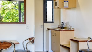 A compact kitchen with a microwave, sink, and a small refrigerator. There are two chairs and a table, and a door leading to another room.