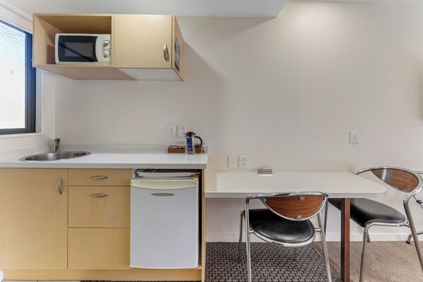 Une petite cuisine équipée d’un four à micro-ondes, d’un évier et d’un lave-vaisselle. On y trouve une petite table avec deux chaises, une fenêtre et un panneau « Interdiction de fumer » sur le mur.