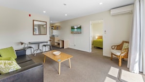 A modern living room with a sofa, a coffee table, a dining area with chairs, a television, and an air conditioning unit.